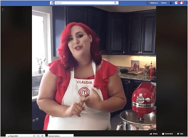 Dette er et screenshot af en Facebook Live-video med kokken Claudia Sandoval, som hun var vært for i 2016 som en del af en krydskampagne med T-Mobile Tirsdags-appen. I videoen står Claudia i et køkken med sorte skabe og granitplader. Et vindue over vasken giver naturligt lys ind i rummet. Claudia står ved siden af ​​en rød køkkenbatteri. Hun er en Latina-kvinde, der har lyst rødt hår, der falder lige under skuldrene. Hun har makeup på, en lys rød top og et hvidt forklæde med Claudia og MasterChef-logoet broderet i rød tråd. Mens hun taler, gestikulerer hun med hænderne. I 2016 samarbejdede Stephanie Liu med Claudia for at producere denne live video.