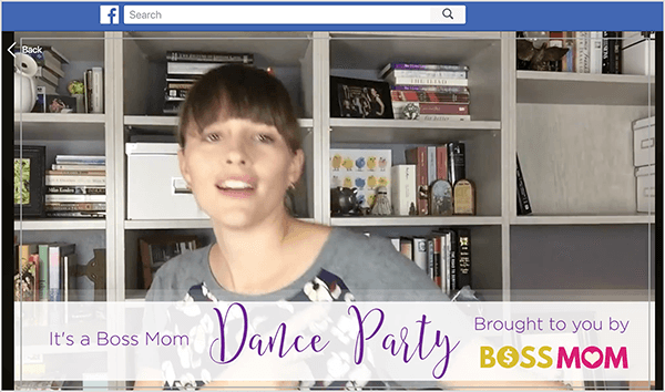 Dette er et screenshot af Dana Malstaff, der danser i en Facebook-video, hun oprettede for at fejre en milepæl i sin Facebook-gruppe. Dana er en hvid kvinde afbildet fra brystet op foran en hvid reol med bøger og hvide arkæsker. Hendes hår er mørkebrunt med pandehår, og resten trækkes tilbage i en hestehale. Et banner nederst i videoen siger: "Det er en Boss Mom Dance Party bragt til dig af Boss Mom."